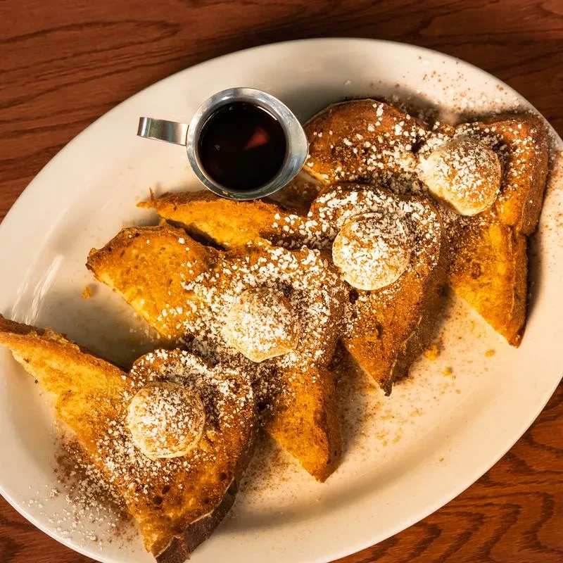 Golden-brown French toast with powdered sugar, butter, and syrup.