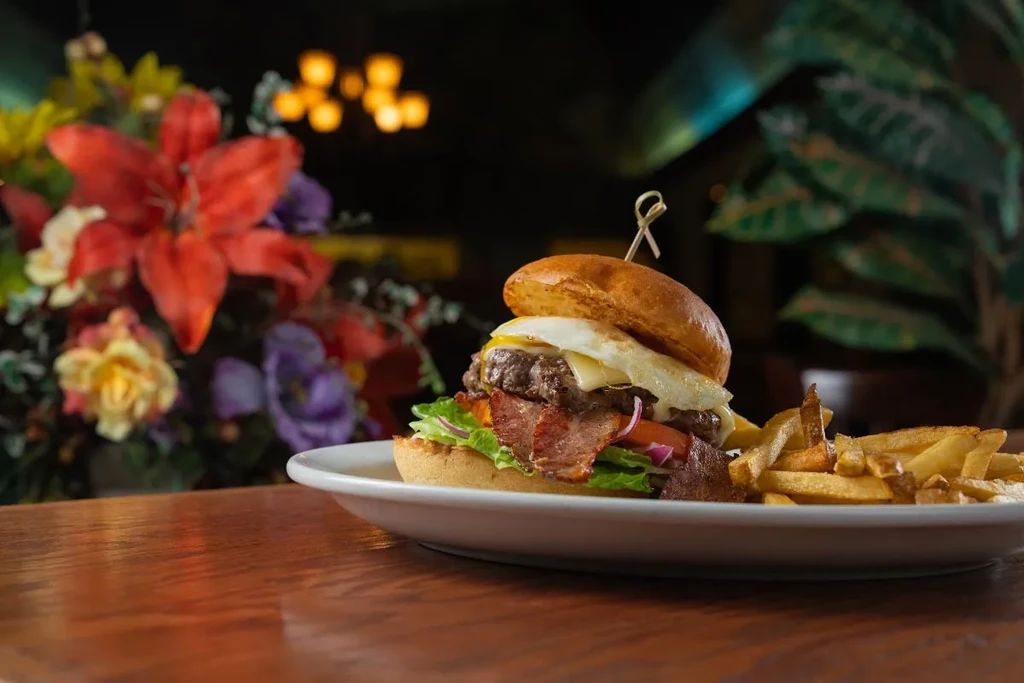 Gourmet burger with bacon, fried egg, and fries, restaurant setting.