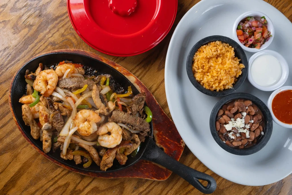 Sizzling mixed fajitas in a skillet with rice, beans, and salsa.