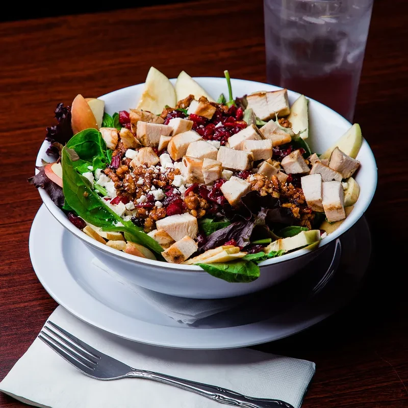 Large colorful salad with chicken, apples, nuts, and feta cheese.