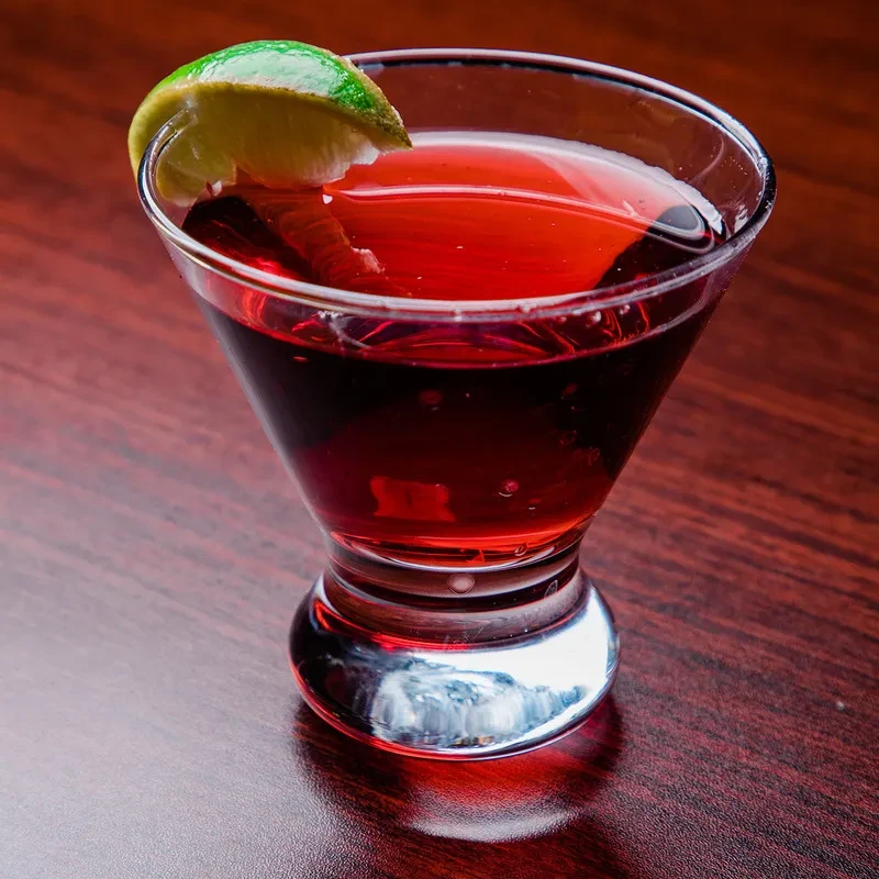 Ruby red drink in martini glass with lime garnish.
