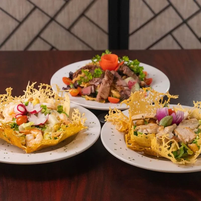 Three plated salads: two in intricate cheese bowls, one steak.
