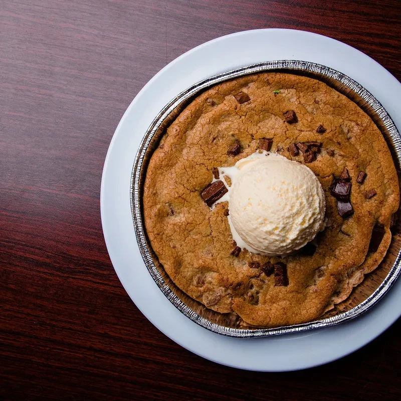 Overhead: Warm chocolate chip cookie in foil pan with melting vanilla ice cream.