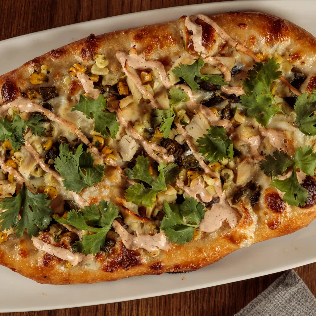 Overhead flatbread with corn, chicken, charred peppers, cheese, sauce, cilantro.