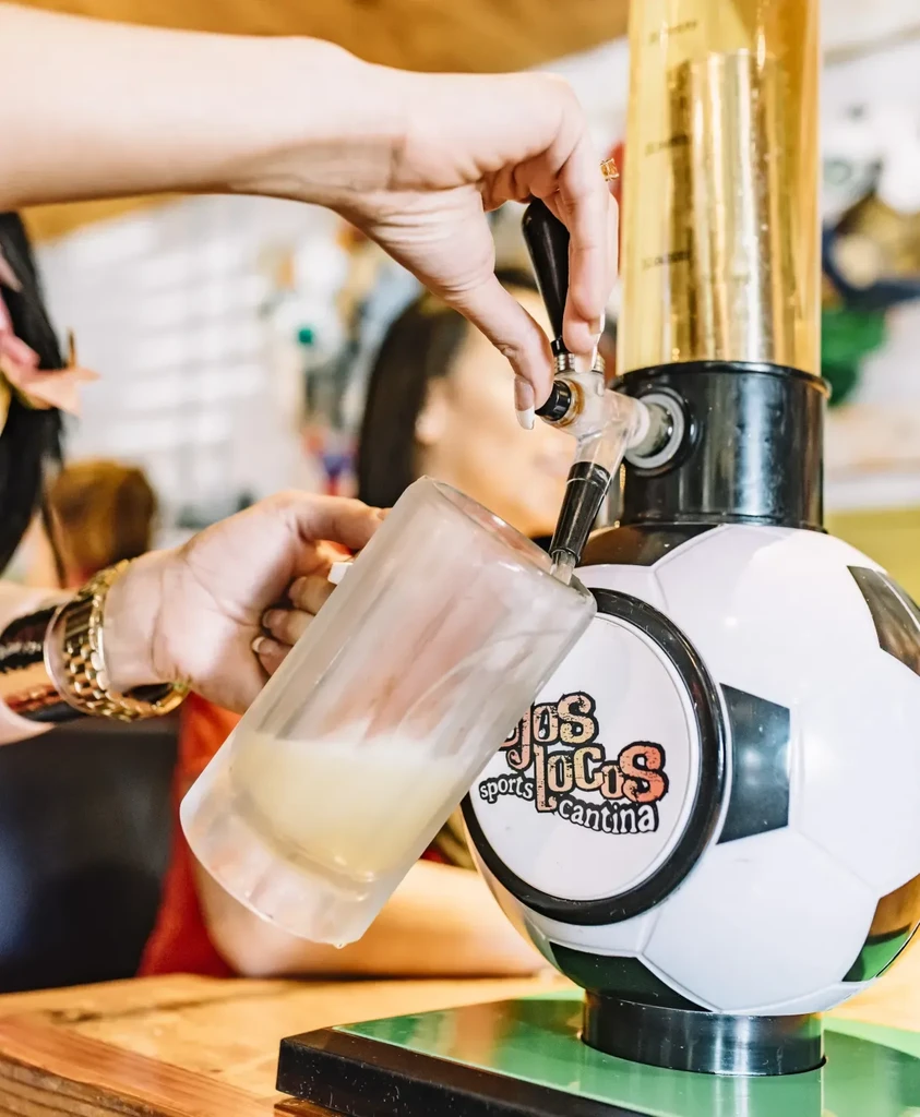 Hands pouring frothy drink from soccer ball dispenser at Jos Locos sports Cantina.