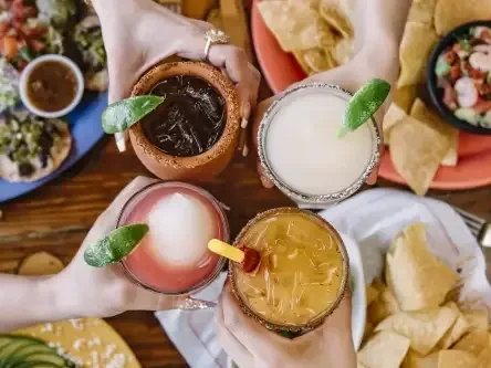 Overhead shot of four distinct garnished drinks held over Mexican food.