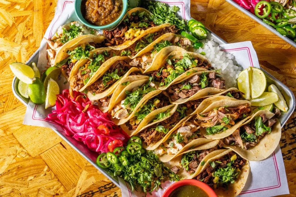 Numerous tacos with various fillings, salsas, and garnishes on a tray.