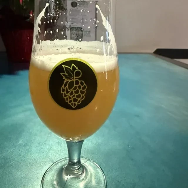 Hazy amber beer with lacing in stemmed glass, hop sticker.