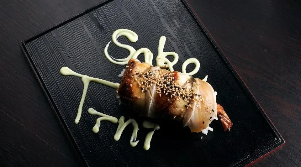 Sushi roll with eel, fried shrimp, and sauce spelling 'Sake Tnt'.