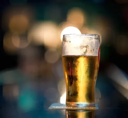 Chilled pint of golden amber beer with foam, in a blurred bar.