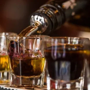 Close-up of whiskey pouring into a shot glass on a bar.