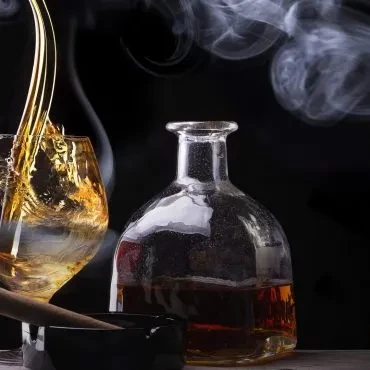 Dark, moody scene: amber spirit poured, bottle, cigar, and smoke.