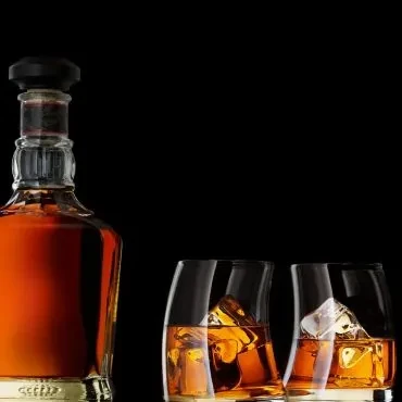 Bottle of amber liquid and two glasses with ice on black.