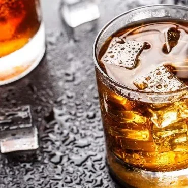 Amber drink in glass with ice cubes, condensation, and wet surface.