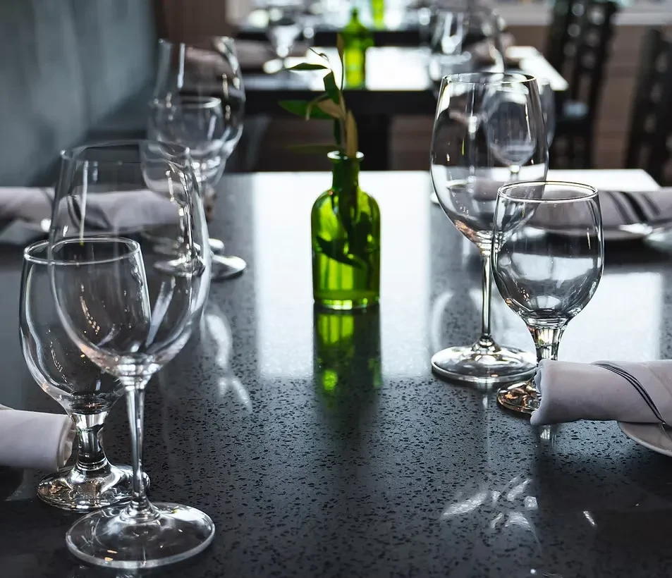 Restaurant table set with glasses, napkins, green vase. No people.