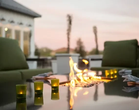 Outdoor fire pit table with candles and lounge chairs at dusk.