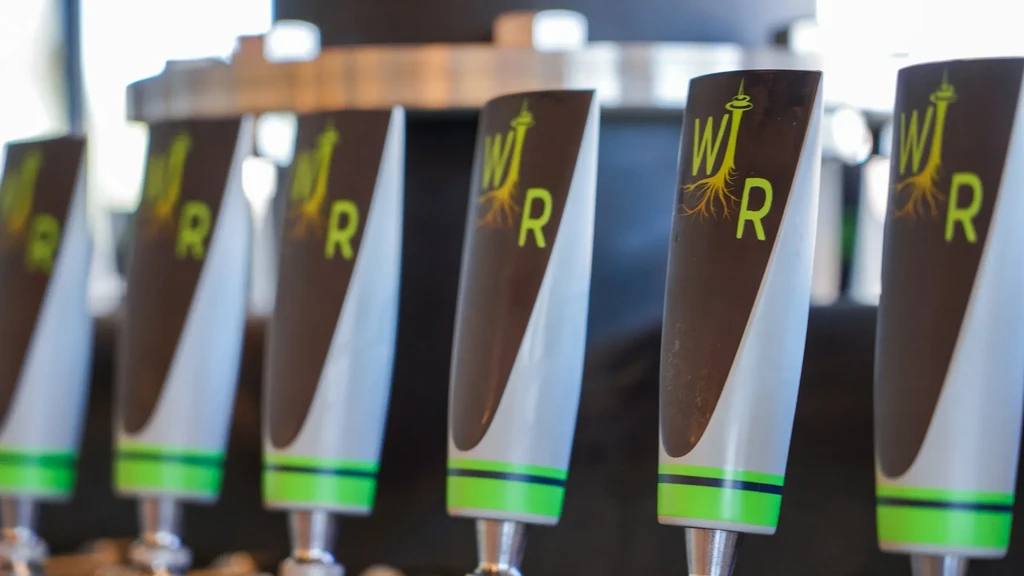Close-up of seven gray-brown beer tap handles with green bands and text.