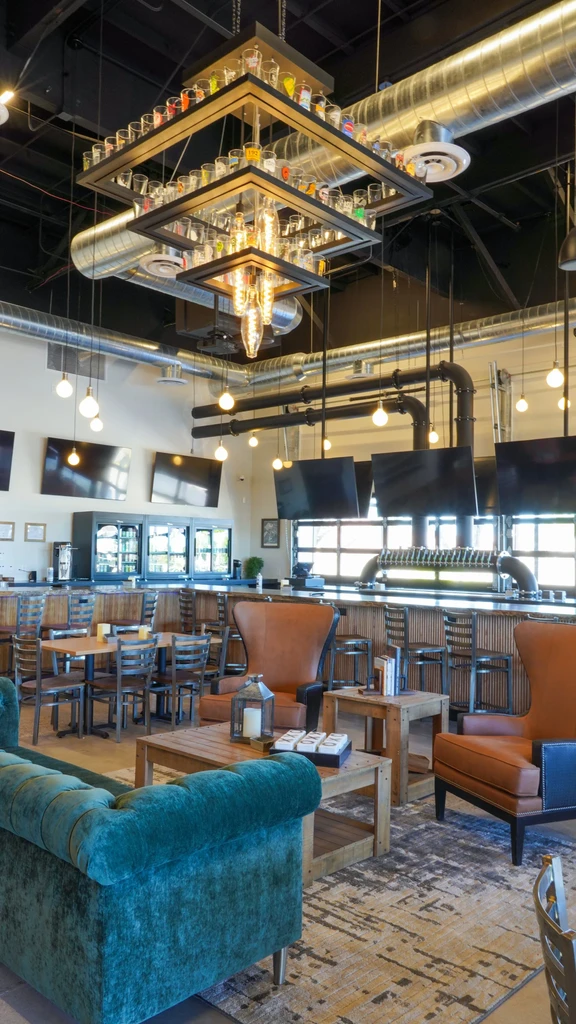 Modern restaurant interior with industrial bar, lounge seating, and glass chandelier.