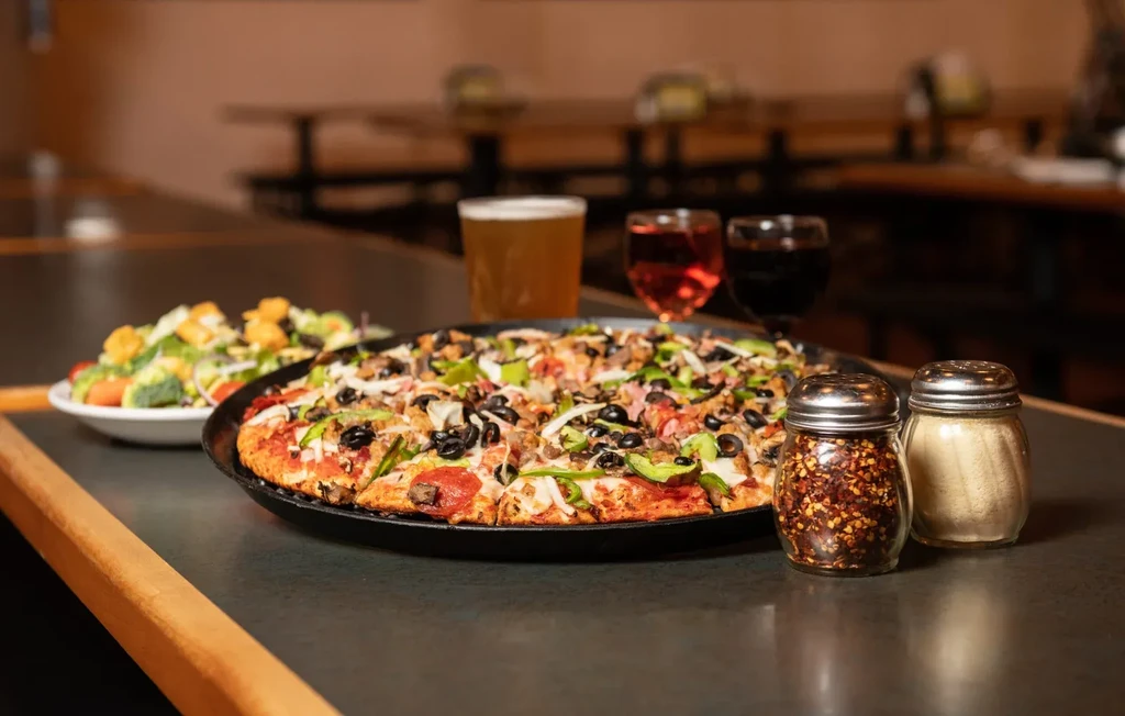 Restaurant table with a loaded pizza, salad, shakers, and beverages.