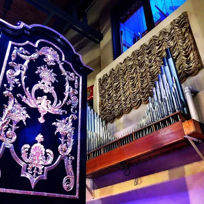 Elaborate rococo panel and pipe organ glowing under blue stage lights.