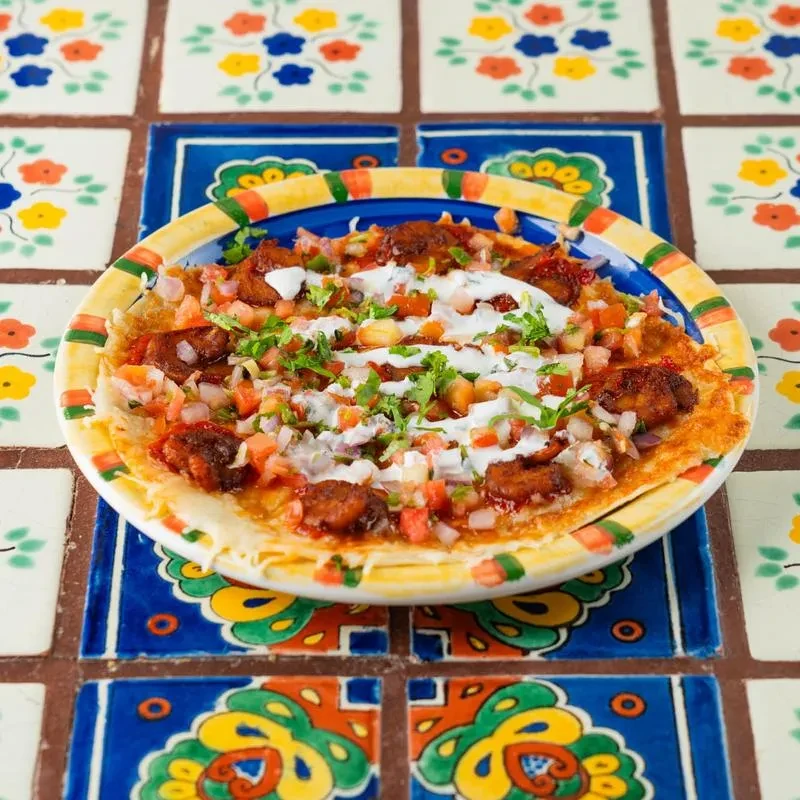 Mexican dish with spiced meat, salsa, and crema on patterned tiles.