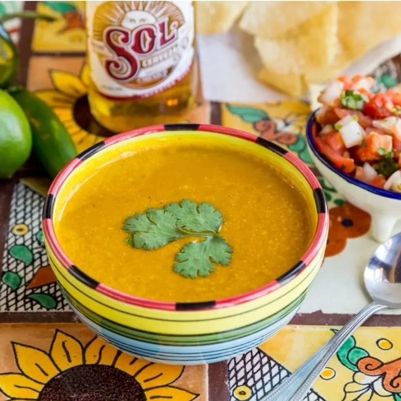 A colorful Mexican meal with creamy soup, pico, chips, and Sol beer.