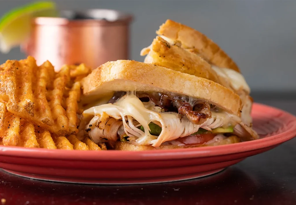Grilled turkey melt with stretching cheese, vegetables, and waffle fries.