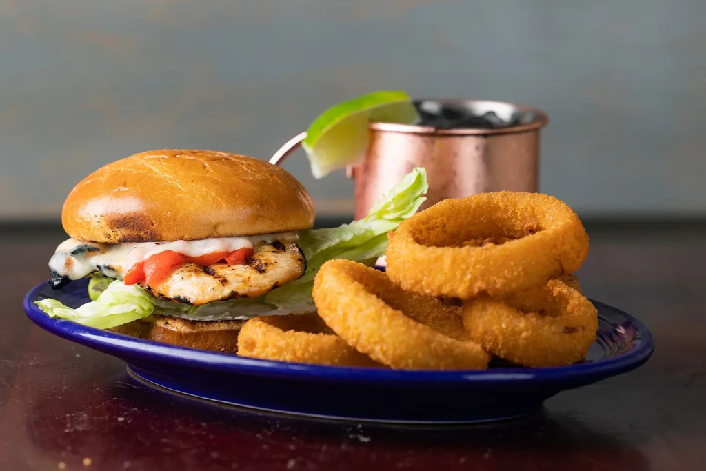 Grilled chicken sandwich with melted cheese, lettuce, peppers, and onion rings.