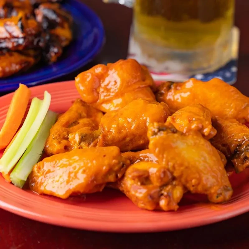 Close-up of glossy orange buffalo wings with celery, carrots, and beer.