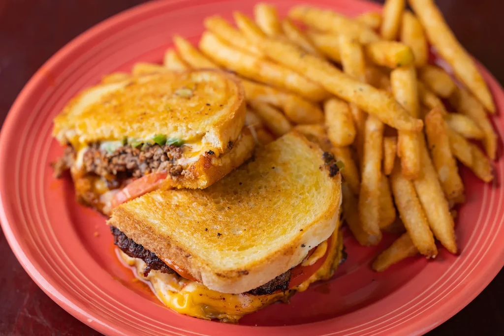 Grilled cheese or patty melt sandwich and fries on a red plate.