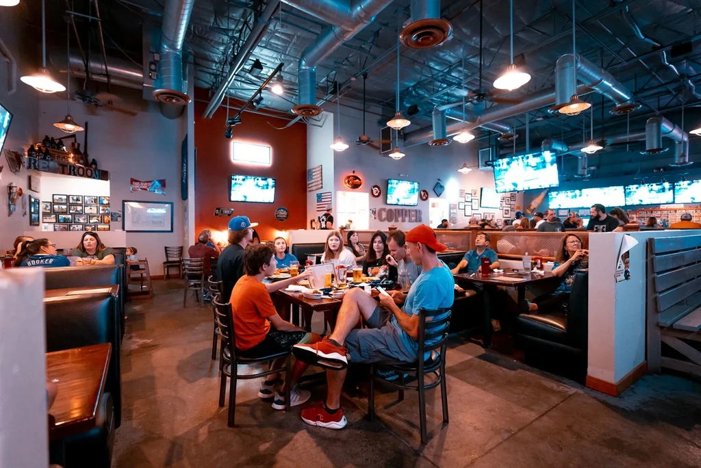 Lively, blue-tinted sports bar interior with industrial design and patrons.