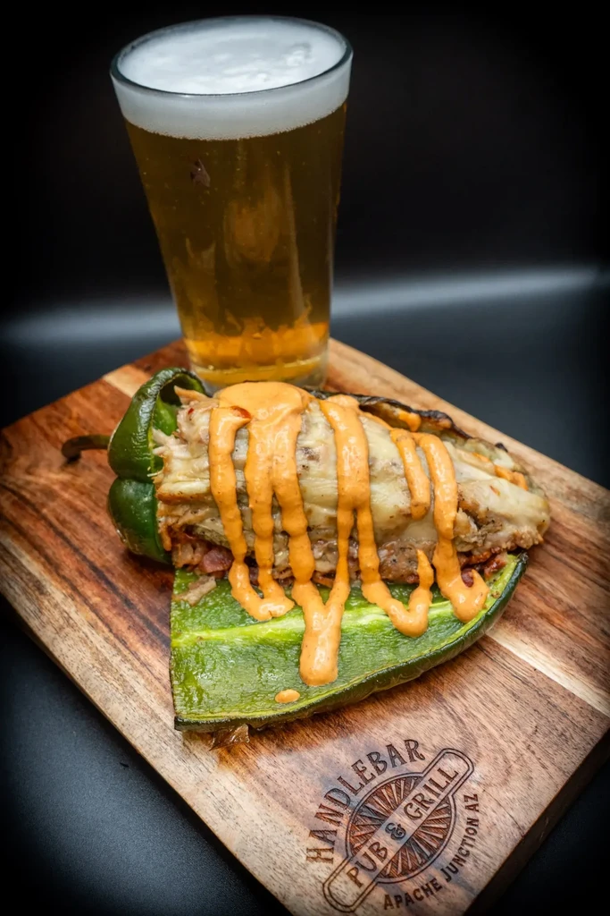 Stuffed green pepper with sauce, beer, served on a rustic wooden board.