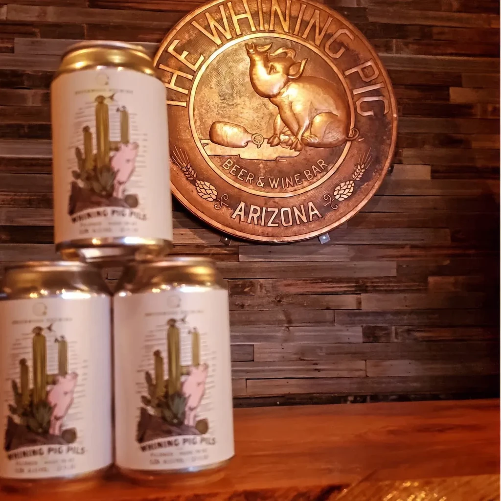 Three Whining Pig beer cans stacked on wood with a matching bar sign.