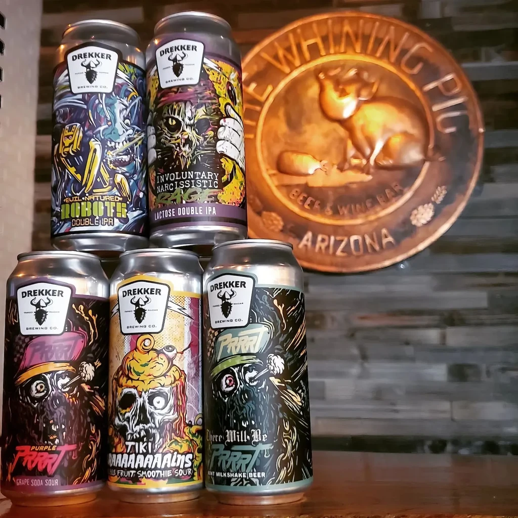 Five colorful Drekker beer cans in a pyramid, before a bar sign.