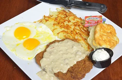 Chicken fried steak, eggs, hash browns, biscuit, and jam on a plate.