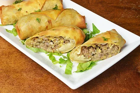 Fried pastries with savory meat filling, garnished with herbs and lettuce.