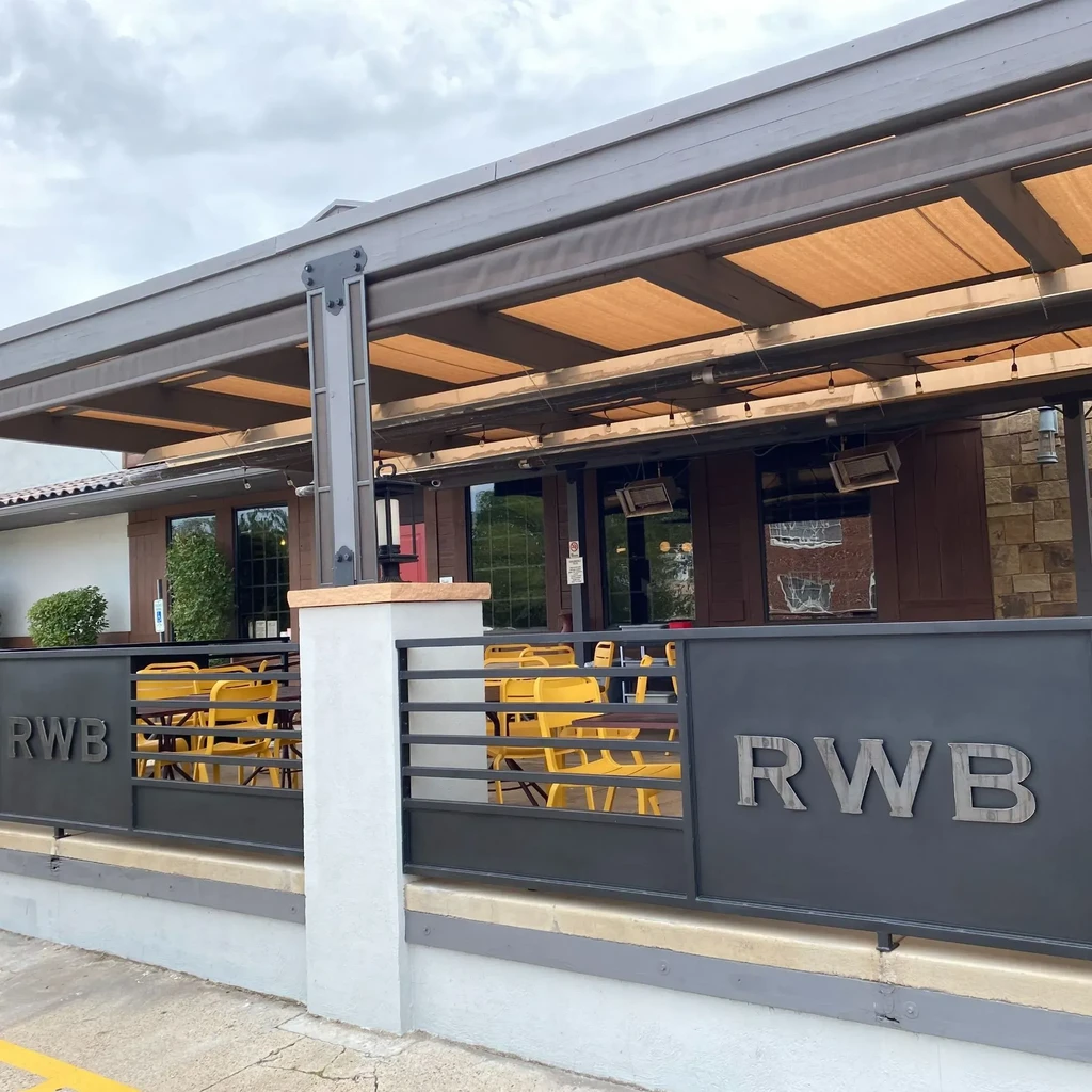 Restaurant patio with grey canopy, yellow chairs, and RWB fence.