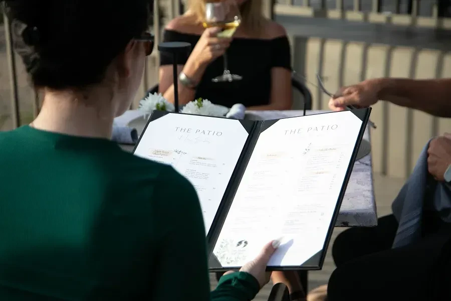 Person reads 'THE PATIO' menu at a sunny outdoor patio.