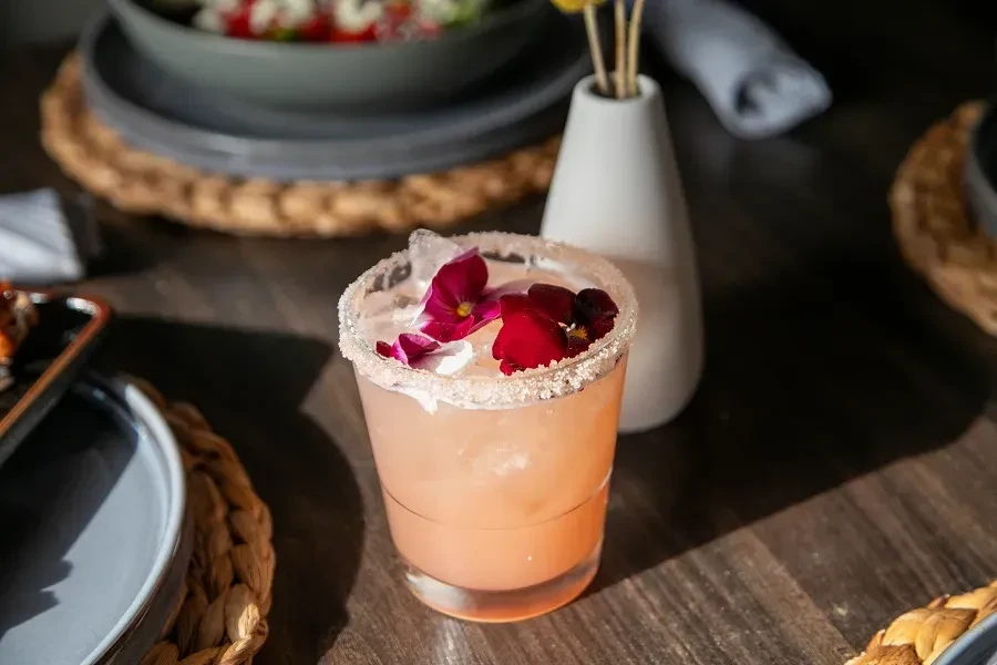Light pink cocktail with sugared rim and red, purple edible flowers.
