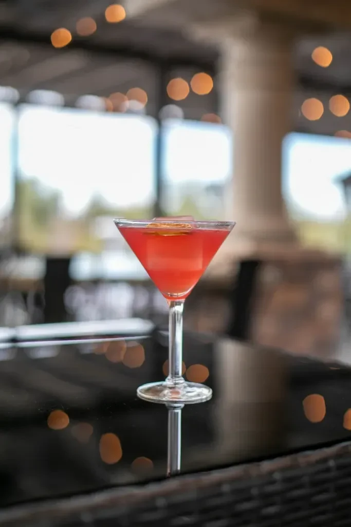 Red cocktail with citrus in martini glass on dark table.