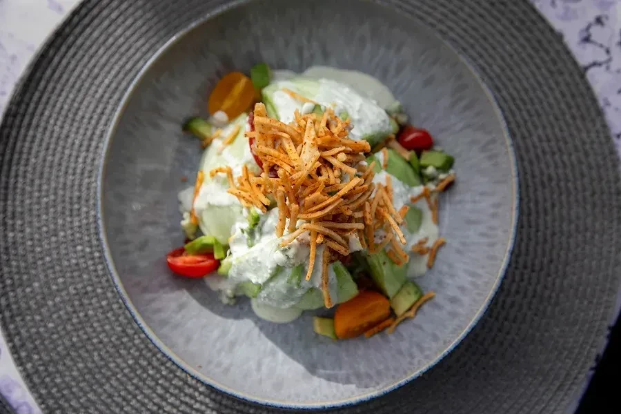 Close-up, overhead salad with avocado, tomatoes, crisps, and dressing.