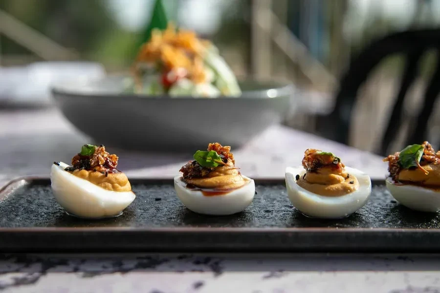 Four deviled eggs topped with caramelized garnish and a green leaf.