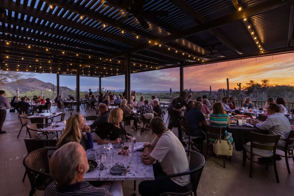 Desert restaurant patio, patrons under string lights, colorful sunset.