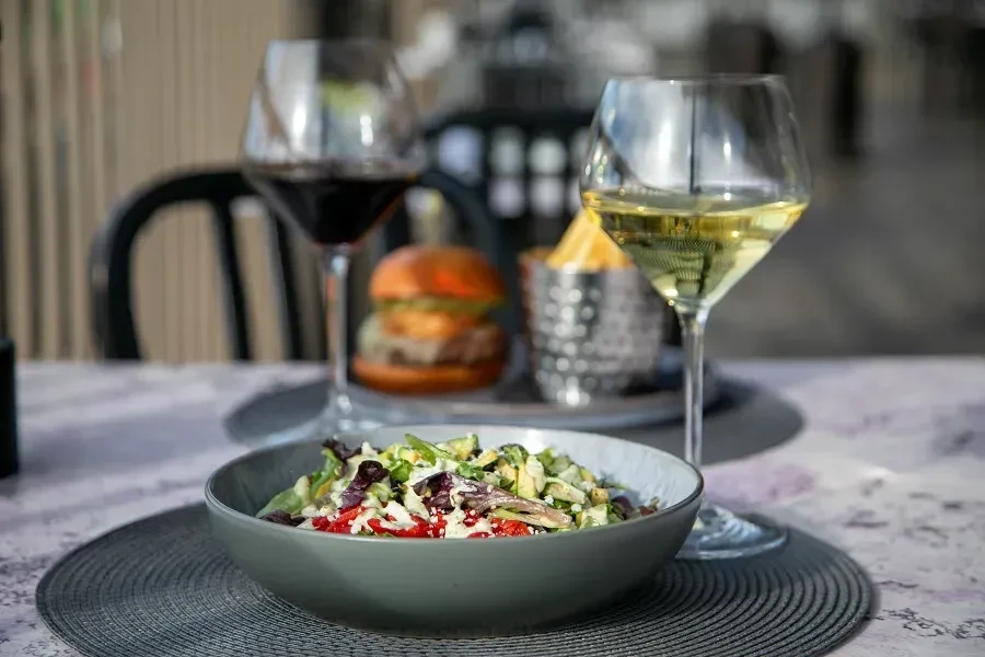 Close-up of a fresh salad bowl, wine glasses, burger, and fries.