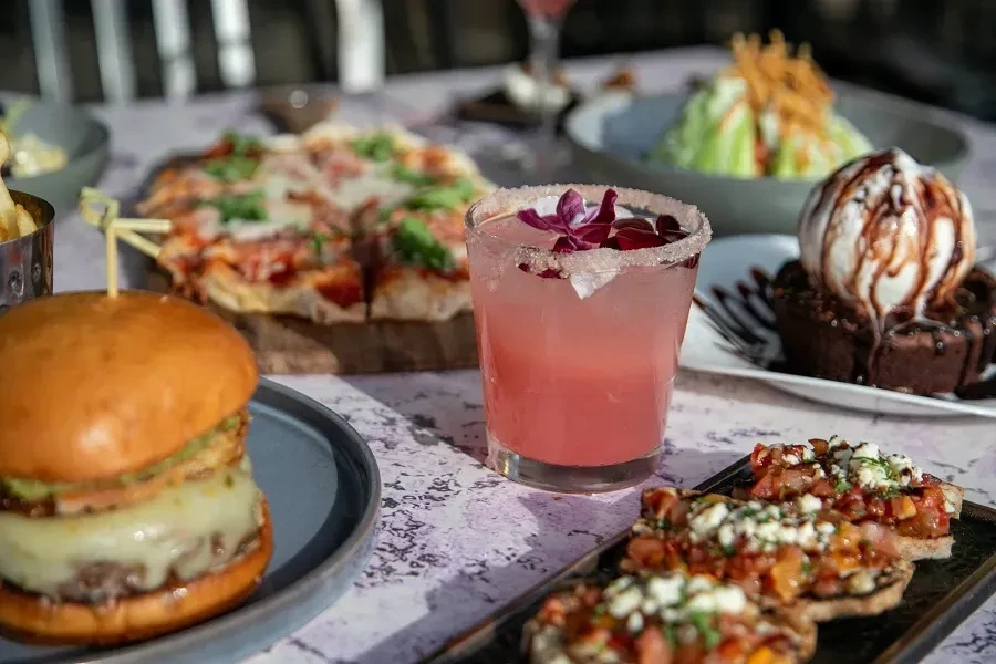 Gourmet burger, cocktail, bruschetta, pizza, and dessert on a restaurant table.