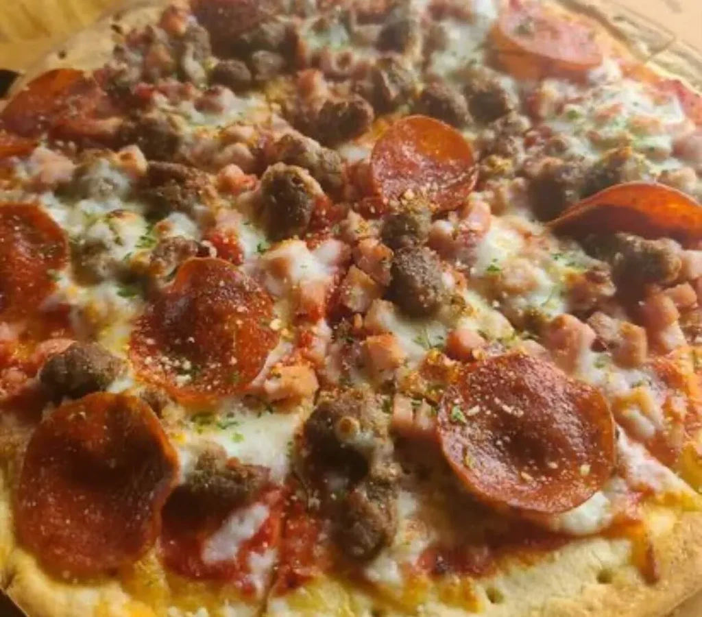 Cooked pizza with pepperoni, sausage, ham, melted cheese, and herbs.