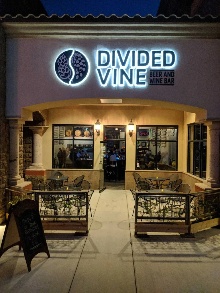 Illuminated Divided Vine Beer and Wine Bar exterior at night with patio.