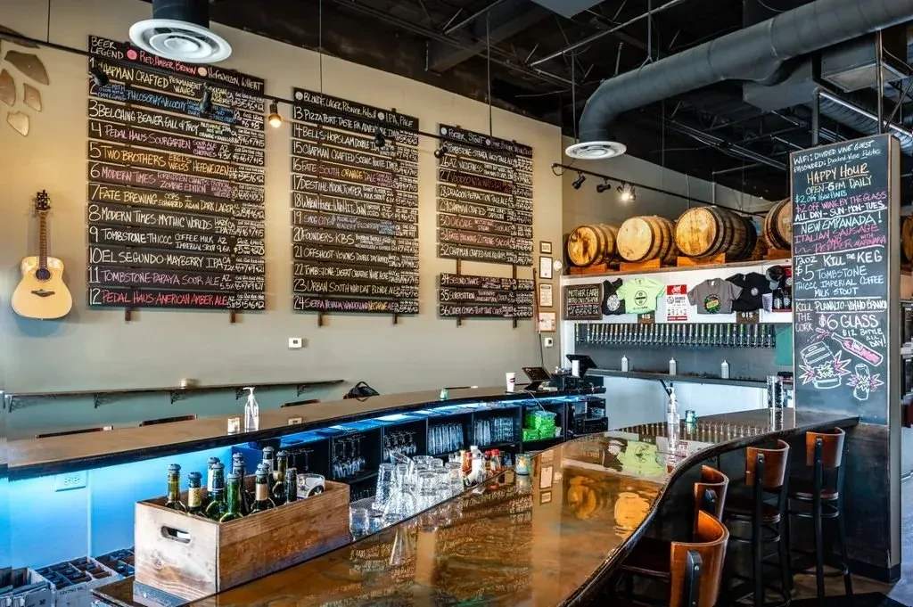 Modern taproom interior with a long bar and chalkboard beer menu.