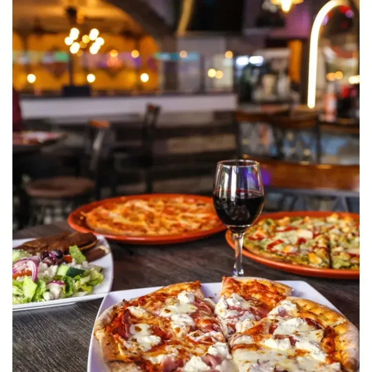 Spread of pizzas, salad, and red wine on a restaurant table.