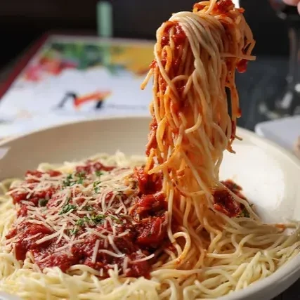 Spaghetti with red sauce, cheese, and herbs lifted high above a bowl.